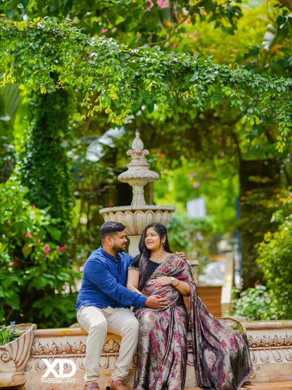 An intimate moment shared by a couple in a lush garden setting, with the mother-to-be in a lovely printed saree.
