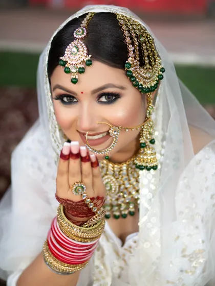 A stunning bride in a white lehenga. The makeup is glamorous, with a smokey eye and a perfectly defined contour, creating a high-fashion bridal look.