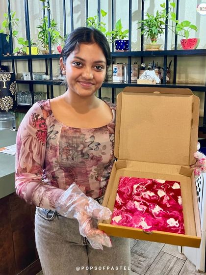 A young woman proudly holds up her beautiful pink and white marbled fluid art canvas from our Women's Day celebration.