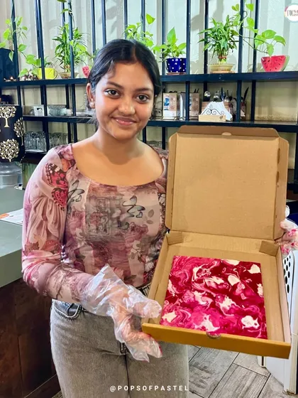 A young woman proudly holds up her beautiful pink and white marbled fluid art canvas from our Women's Day celebration.