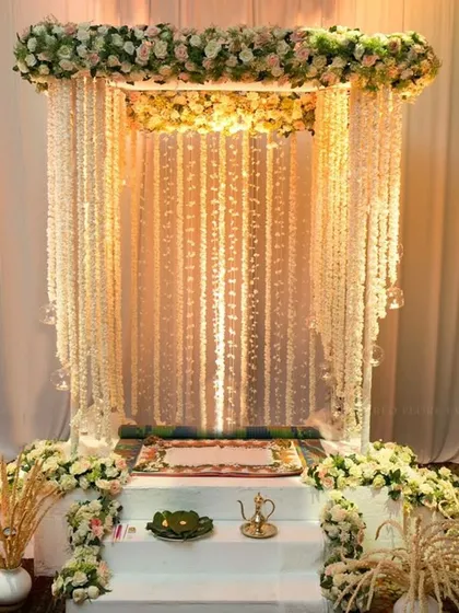 I create serene and beautiful mandaps for Navratri. This elegant setup features a canopy of white and pink flowers with hanging floral strings, creating a divine space for pooja in your home.