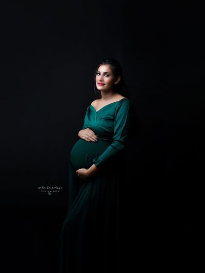 A simple, elegant portrait in a beautiful emerald green gown. The focus is entirely on the mother-to-be and her gentle hold on her bump.