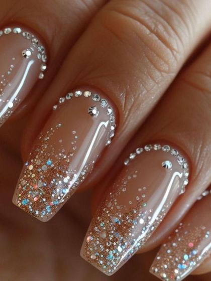 Nail inspiration for a glamorous look with a nude base, glitter ombré, and a full border of rhinestones.