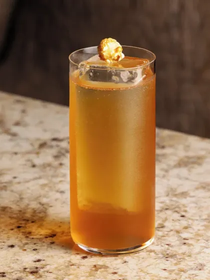 A movie-night inspired highball, this drink is garnished with a single piece of caramel popcorn, adding a touch of whimsy and flavor.