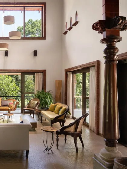 In the living room of the Dream Coffee Estate, a reclaimed antique wooden column stands as a silent witness to time, grounding the double-height space. We designed this room to be a conversation between old and new, where hand-chiseled stone floors and modern furnishings coexist under the expansive canopy of the Coorg forest visible through large glass doors.