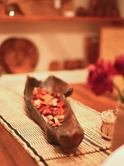 This rustic, hand-carved wooden bowl is filled with potpourri, serving as a beautiful and fragrant centerpiece for a dining or coffee table. Its organic shape adds a touch of nature.