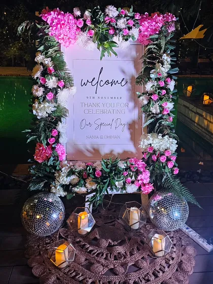 An elegant floral welcome sign for an anniversary party, surrounded by disco balls and candles. This setup combines romantic and fun elements for a unique look.