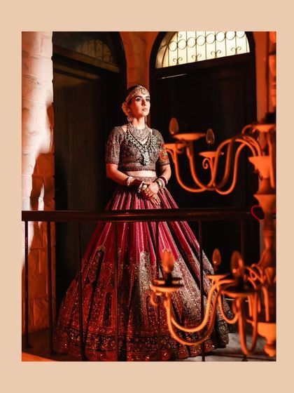 The bride poses with regal confidence on a balcony, her grand lehenga framed by an ornate candelabra.