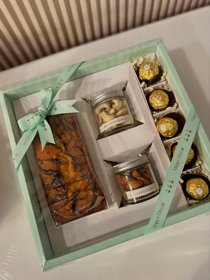 Simple, elegant, and delicious. This Celebration Box features a decadent marble tea cake, jars of premium almonds and cashews, and Ferrero Rocher chocolates, all beautifully presented in a pastel box with a custom Diwali ribbon.