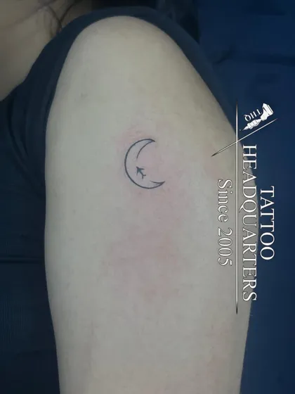 A tiny minimalist tattoo of a crescent moon with an airplane flying across it, perfect for a traveler.