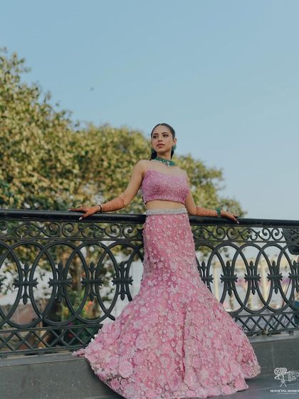 A full-length portrait of the bride in her stunning pink floral gown. Her confident pose on the bridge, with the sky as her backdrop, creates a modern and powerful bridal image.