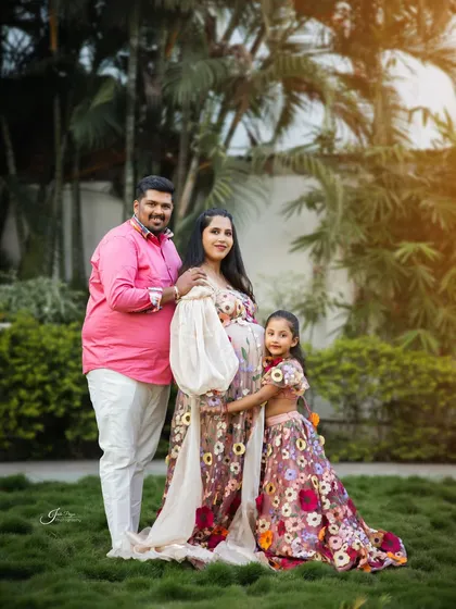 An outdoor maternity shoot celebrating the complete family. The parents and soon-to-be big sister are coordinated in beautiful floral outfits, capturing a moment of togetherness in a lush, green setting.