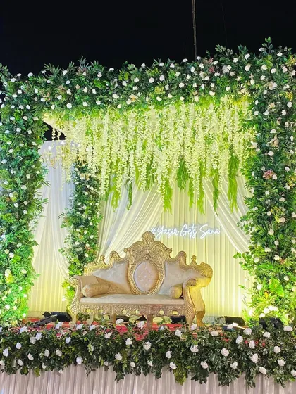 A full view of the greenery arch stage, showing the lush floral border and the elegant gold and white seating.