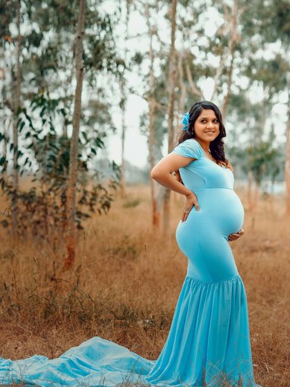A beautiful profile shot of this mom-to-be in a flowing blue gown. The outdoor setting adds a touch of natural elegance to the portrait.