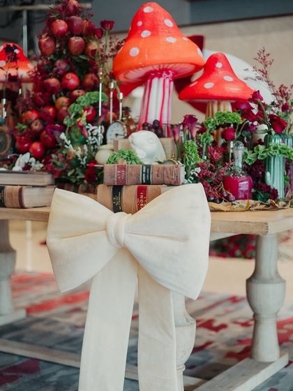 A fantastical tablescape with oversized mushrooms, vintage books, and a large white bow, capturing the surreal magic of Alice in Wonderland.