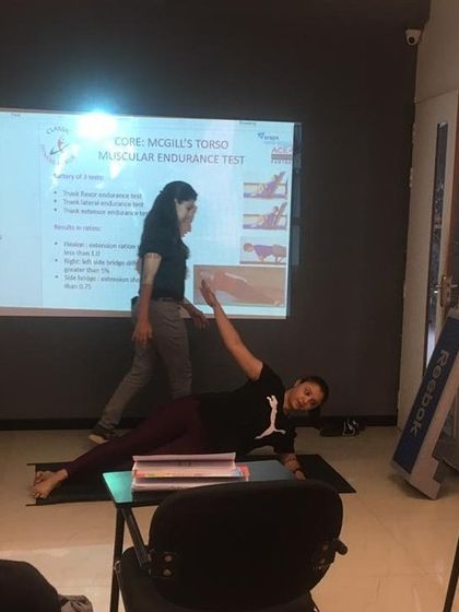 Our theory classes are interactive. A student demonstrates a core endurance test while the trainer explains the muscular engagement to the class.