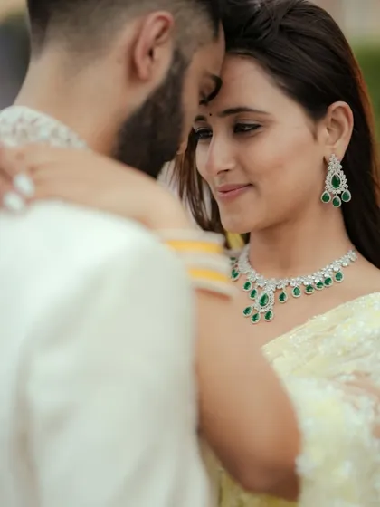 An intimate close-up capturing a quiet moment of connection. The focus on the couple's expressions and the elegant details of their attire, like the emerald jewelry, makes this a powerful cinematic portrait from a Mumbai engagement shoot.