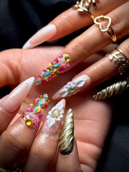 A close-up of the detailed nail art, showing the combination of French tips, 3D florals, and textured gold nails.