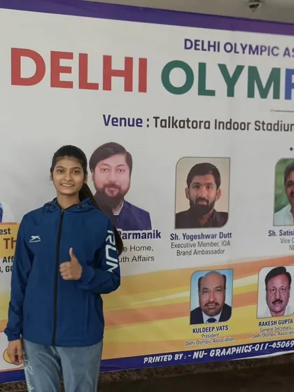 One of our students at the Delhi Olympic Games 2024, standing proudly before the event banner.
