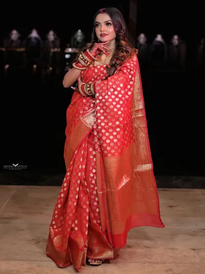 A full-length portrait showcasing the elegance of the red Banarasi saree against a dark background.