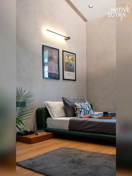 This loft-style bedroom features a low-profile bed and minimalist decor to maximize the sense of space. The concrete-textured walls are complemented by modern art and a sleek wall lamp, creating a cool, urban aesthetic.