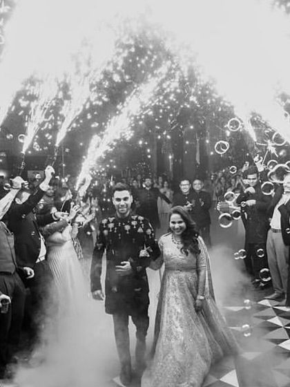 A dramatic, black and white shot of the couple's Sangeet entrance, surrounded by guests, bubbles, and cold pyro fireworks for a spectacular welcome.