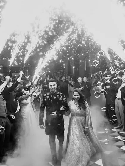 A dramatic, black and white shot of the couple's Sangeet entrance, surrounded by guests, bubbles, and cold pyro fireworks for a spectacular welcome.