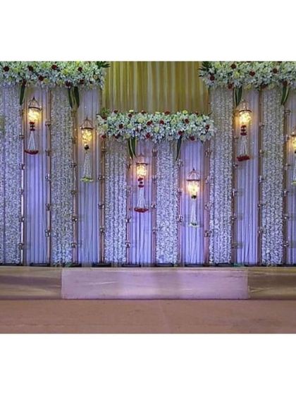 This backdrop features vertical panels of white flowers and hanging traditional lanterns. It's a unique and sophisticated design that adds texture and warm light to the main stage area.