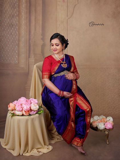 A regal studio portrait of a mother-to-be in a traditional Maharashtrian-style nauvari saree, seated gracefully with floral props.