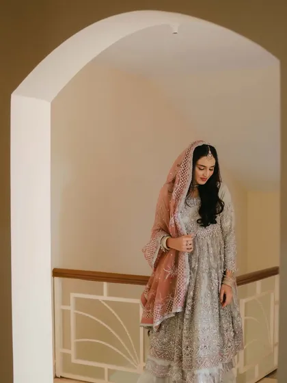 A thoughtful portrait of the bride, her expression serene as she adjusts her dupatta, framed beautifully within a doorway.