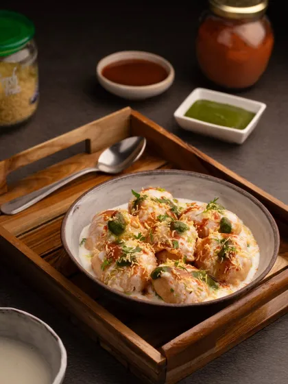 A beautifully styled bowl of Dahi Vada. The dark, moody lighting and wooden tray give this classic chaat a sophisticated look.