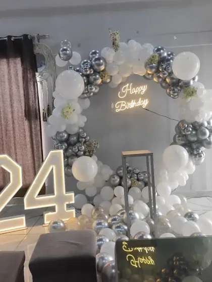 A chic silver and white theme is used here to celebrate a 24th milestone. The illuminated marquee numbers are a key feature, complementing the neon sign and circular balloon backdrop for a modern party look.