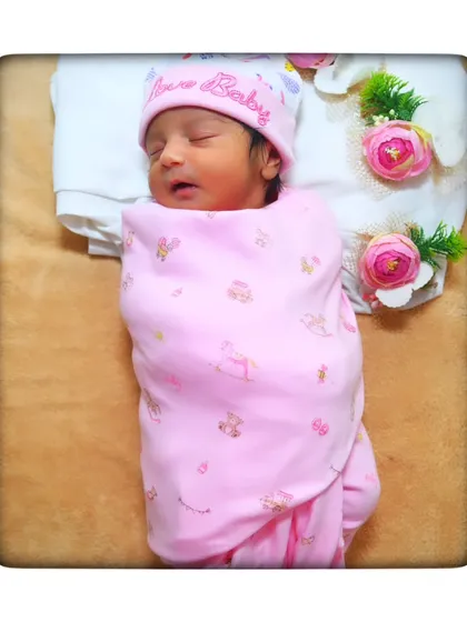 This little one is all bundled up in a pink swaddle and matching hat, ready for a nap. The floral props add a touch of spring.