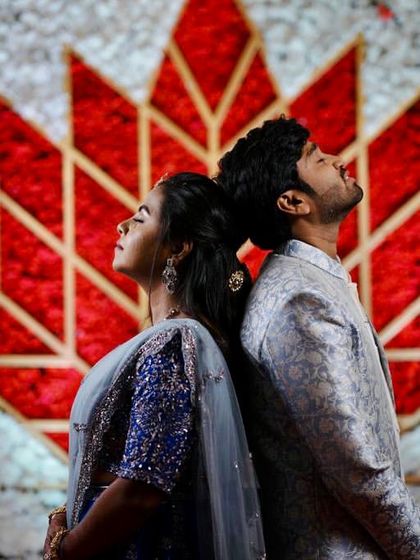 A creative and artistic shot of a couple posing against a custom floral backdrop. The backdrop features a large lotus motif made of red and white flowers, providing a unique and memorable photo opportunity.