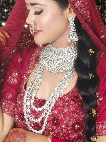 A bride wearing a heavy, layered American Diamond set with her red lehenga. The braided hairstyle with accessories completes this glamorous look.