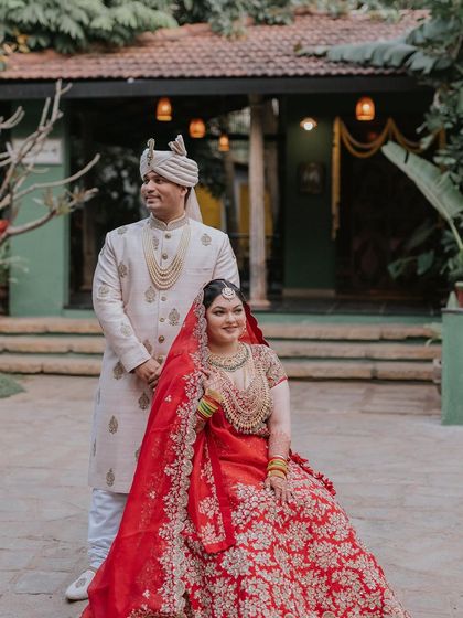 A bride in a magnificent red lehenga, ready for her big day, posing in the courtyard.
