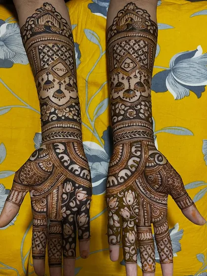 An elegant engagement mehendi design. The back of the hands features jhumka (earring) motifs and the couple's initials, while the palms have a floral and lotus pattern.
