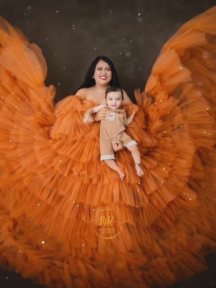 A mother and her baby seem to float on a cloud of orange fabric, creating a whimsical and angelic portrait.