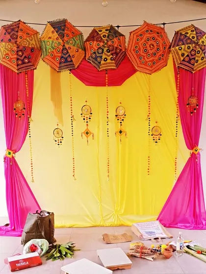 A vibrant Haldi ceremony backdrop. The combination of bright yellow and pink drapes, along with decorative Rajasthani umbrellas, creates a festive and photo-ready setting for the celebration.