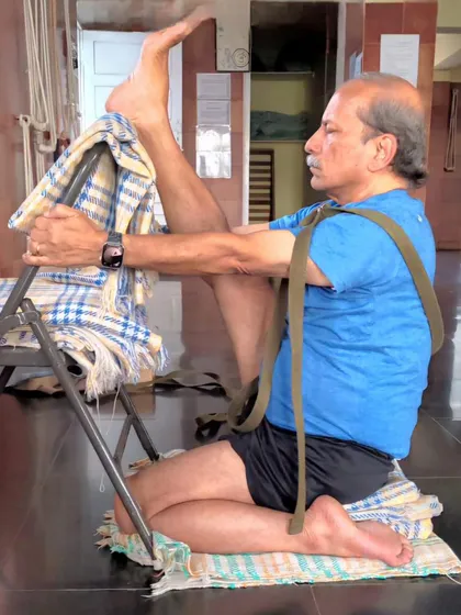 Using a chair and strap to work on hip and hamstring flexibility in a seated position. This is a preparation for poses like Krounchasana (Heron Pose).