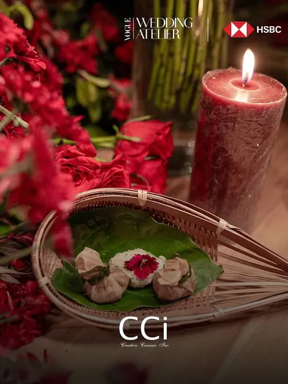Setting the mood is an art form. This atmospheric shot from the Vogue Wedding Atelier captures a moment of quiet luxury, with traditional paan presented on a betel leaf against a backdrop of rich red florals and candlelight.