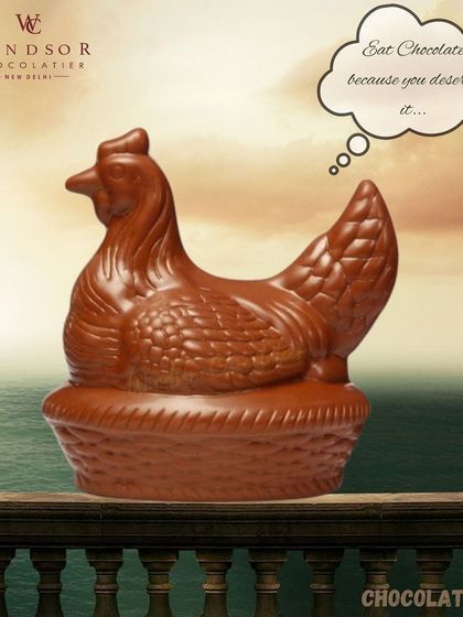 A realistic chocolate hen sitting in a basket, crafted entirely from rich milk chocolate with detailed feathers.