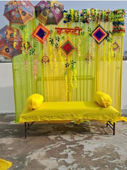 A simple and sweet Haldi seating arrangement for a terrace or backyard. The light yellow drapes are decorated with phulkari umbrellas and floral vines, creating a lovely photo opportunity.