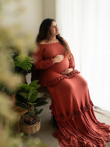 A thoughtful pose by the window. The way the light falls on her and the flowing gown creates a beautiful, contemplative maternity portrait.