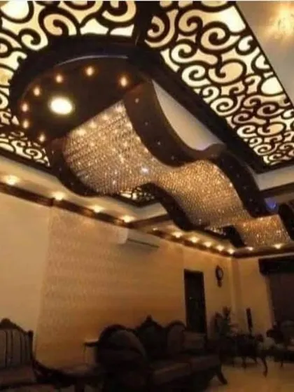 A truly breathtaking ceiling design featuring a massive, wave-like crystal chandelier set against a dark, curved structure with backlit jali work. This is the pinnacle of luxury.