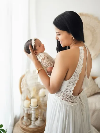 A mother holds up her newborn baby, sharing a look of pure love. The intricate lace on the mother's dress adds a beautiful detail to this portrait.