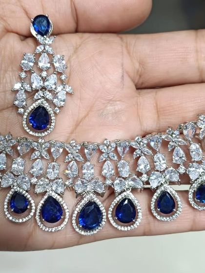 A close-up of a delicate American Diamond necklace with sapphire-blue stones. I have AD sets in all polish types and colors.