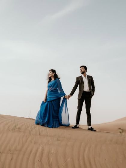 The sweeping dunes of the desert create a dramatic and romantic setting. The bride's flowing blue saree provides a stunning contrast against the sand.