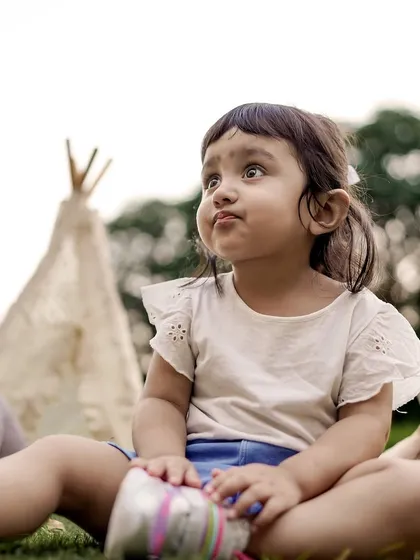 A curious little girl sits among her teddy bears during a teepee-themed picnic setup in a park.
