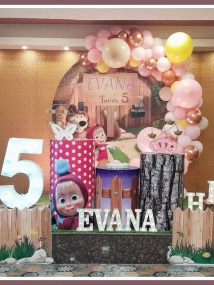 A charming Masha and the Bear-themed fifth birthday. The setup includes a woodland backdrop, character-printed plinths, and a large light-up number '5'.